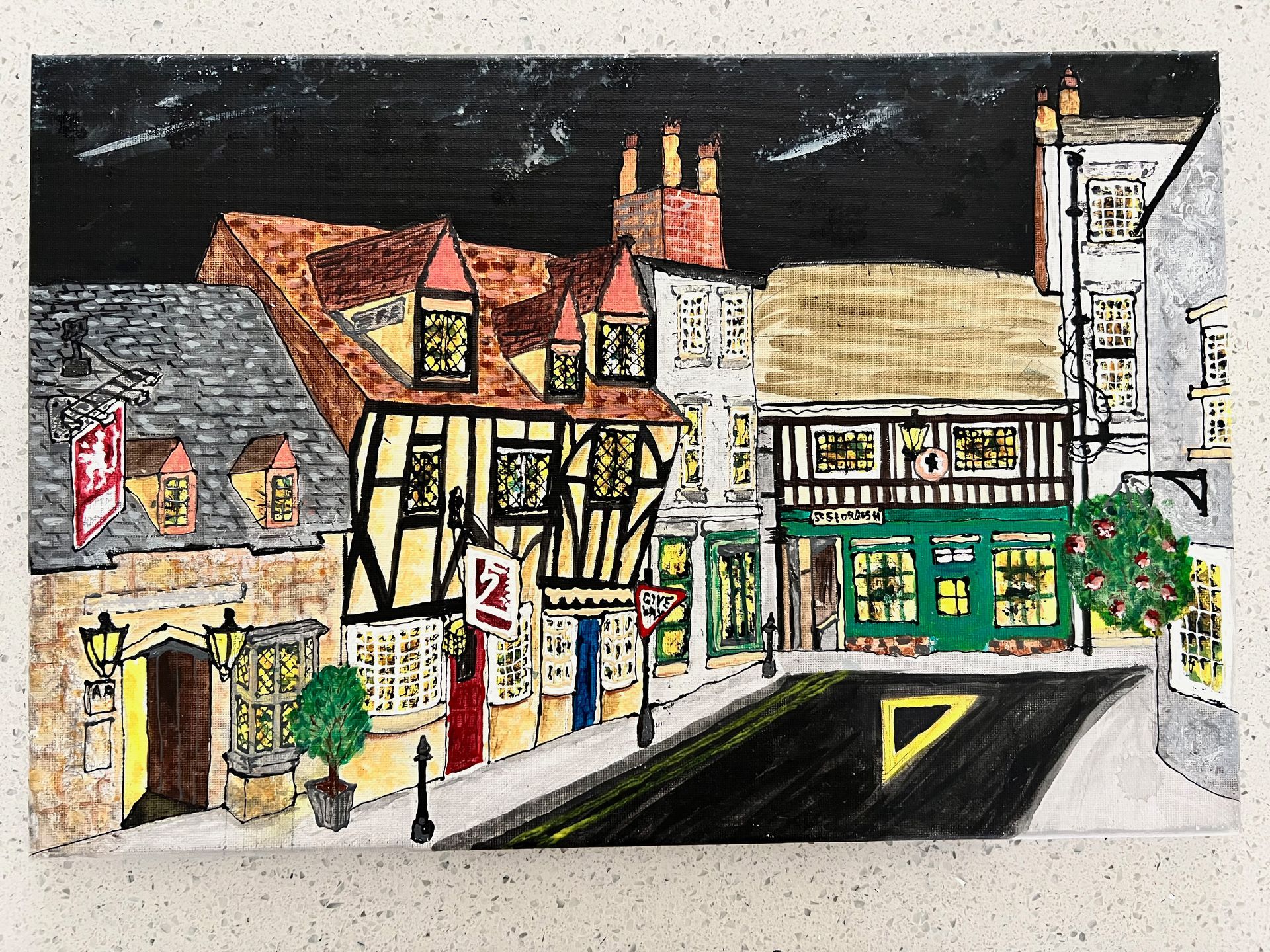 Town street scene with half-timbered buildings, lit windows, a road, and a dark, starry sky.