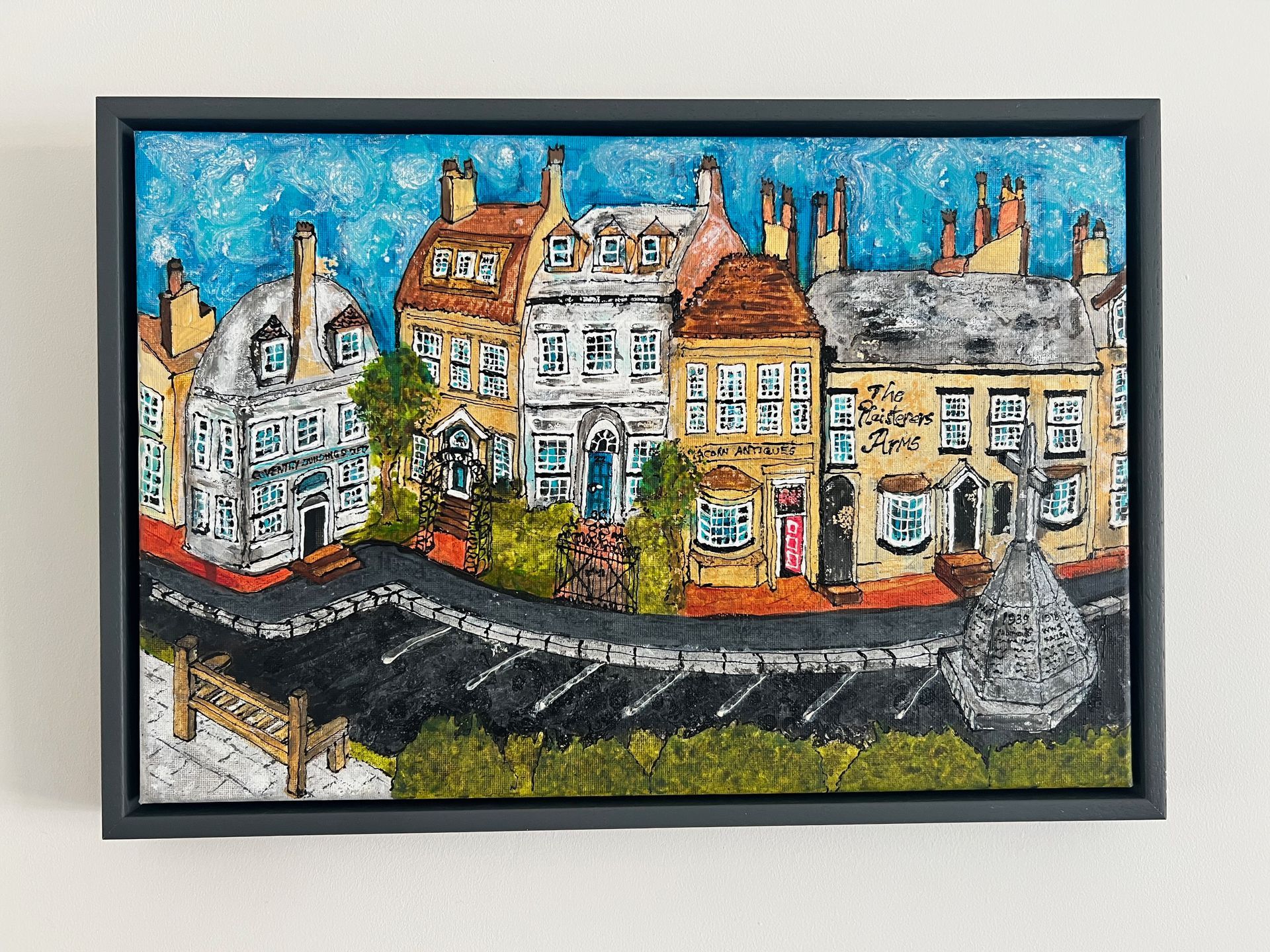 Row of colorful townhouses with a winding road, blue sky background, and a grey framed picture.