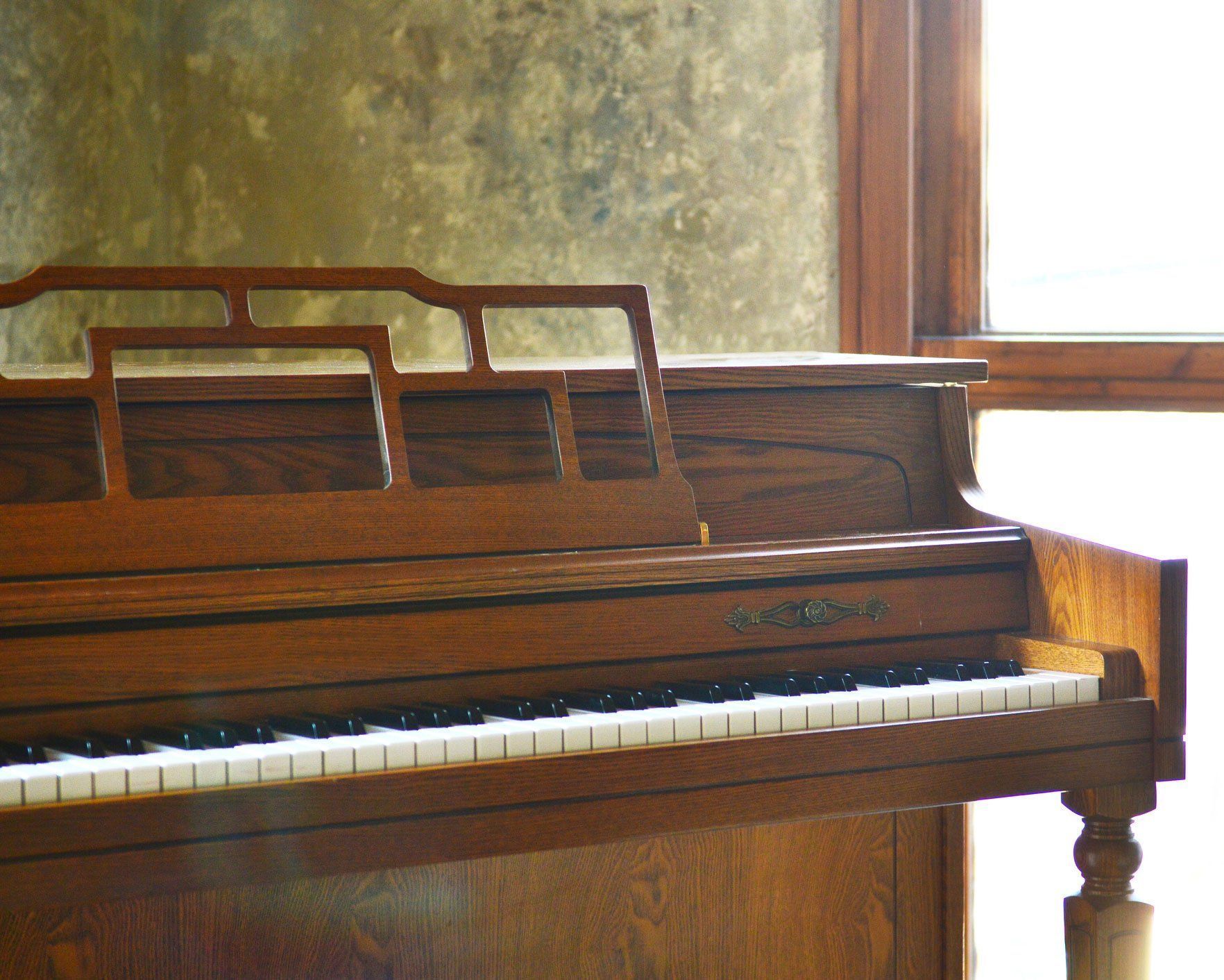 A wooden piano is sitting in front of a window