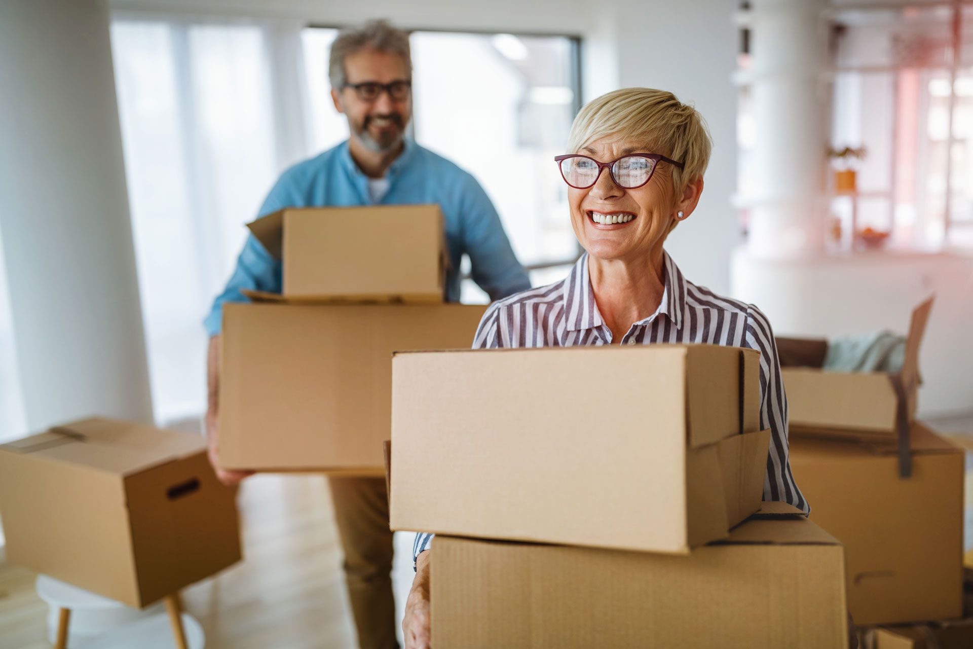 Couple carrying cardboard boxes, smiling, moving into a new home.