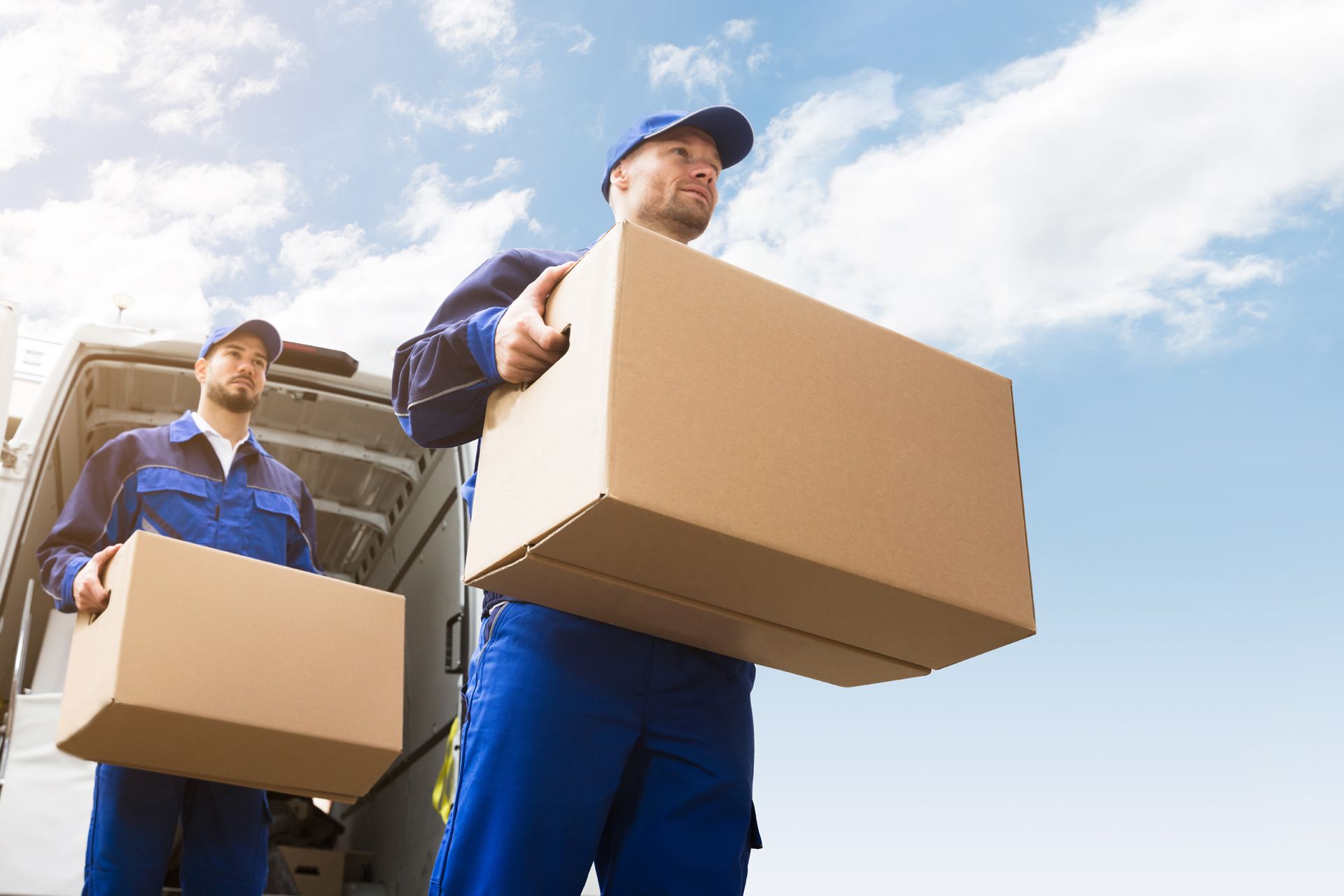 Two delivery men are carrying boxes out of a truck