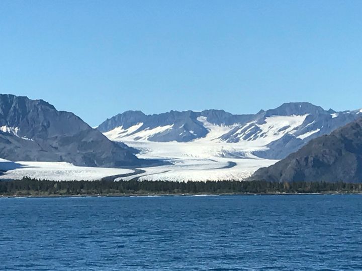 Snow-covered mountains and glacier behind a blue lake under a clear sky