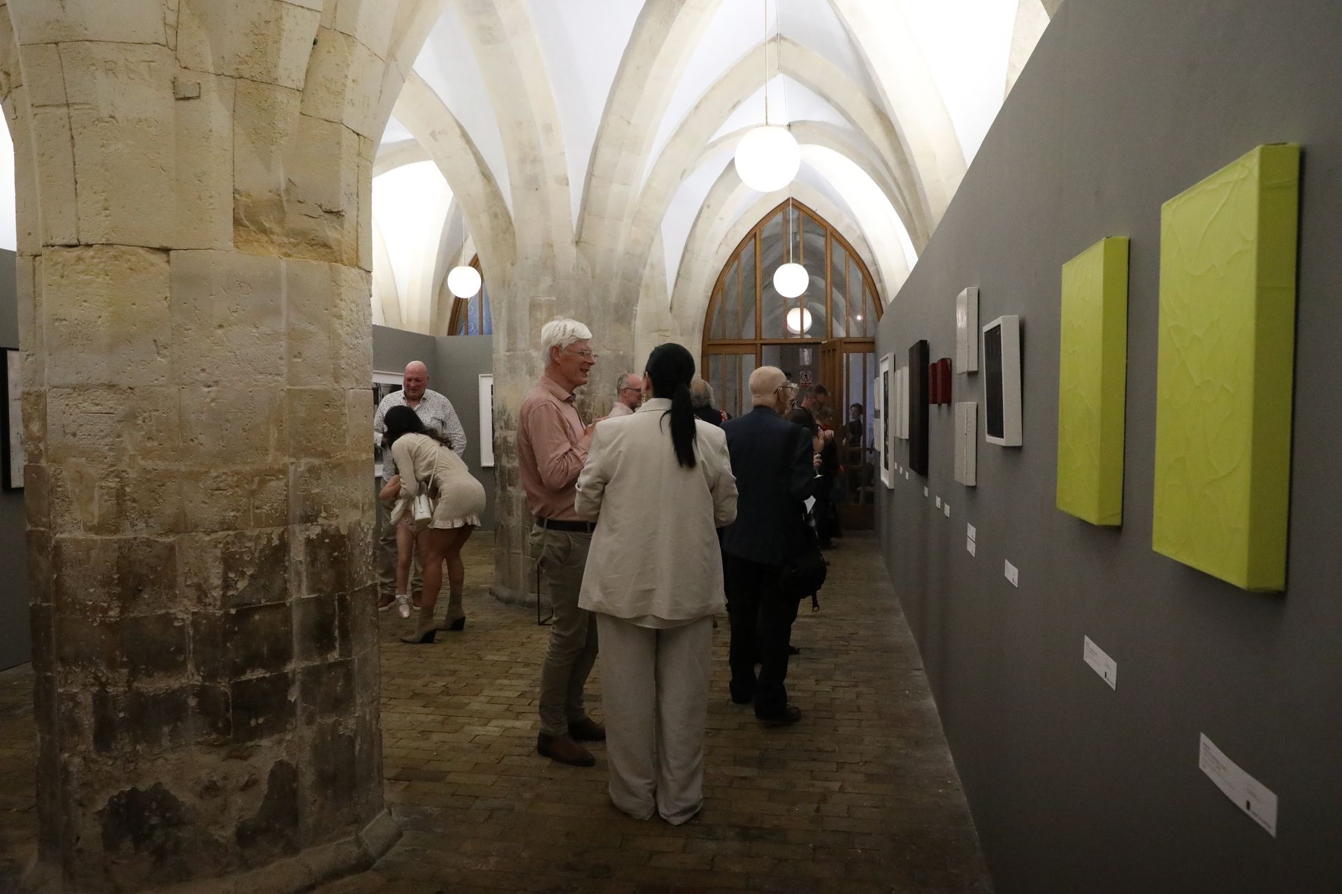 A group of people are standing in a hallway looking at paintings on the wall.
