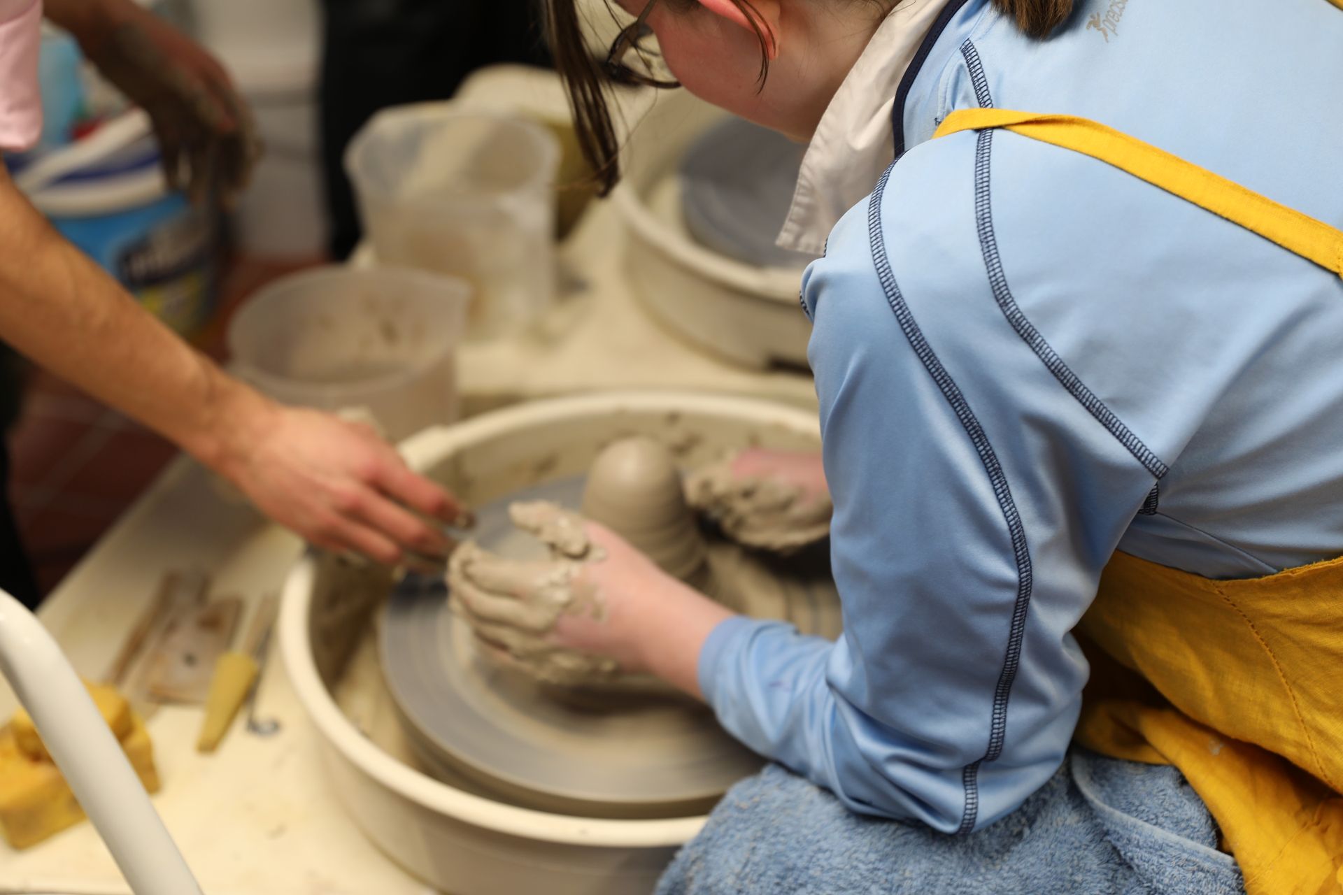 A woman in a blue shirt is working on a pottery wheel
