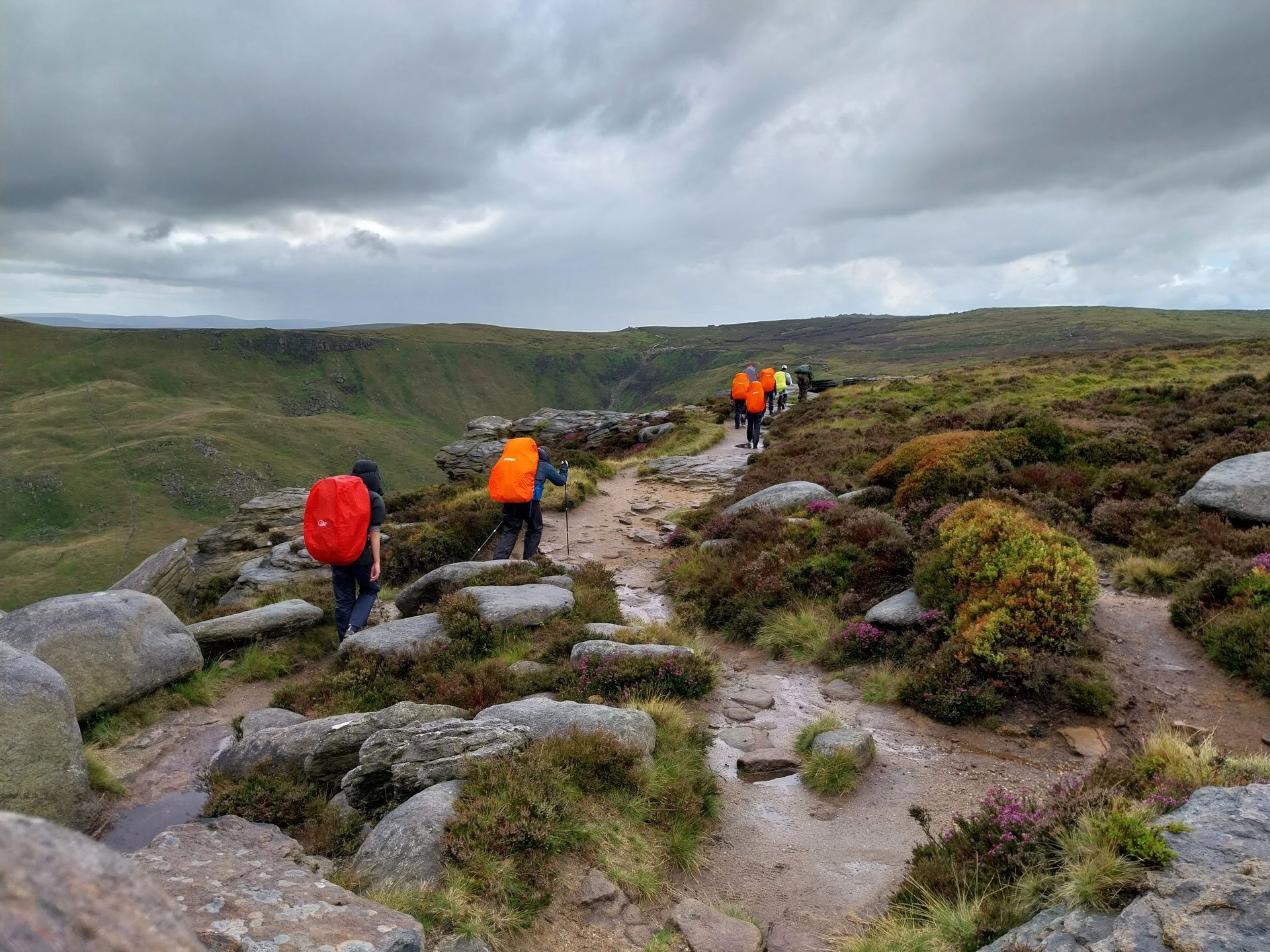 A group of people with backpacks are walking down a path in the mountains.