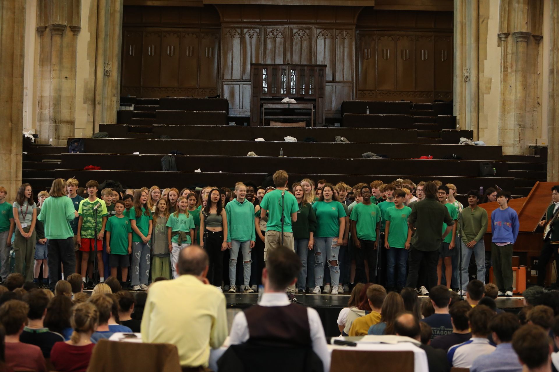 A large group of people in green shirts are standing in a large auditorium.