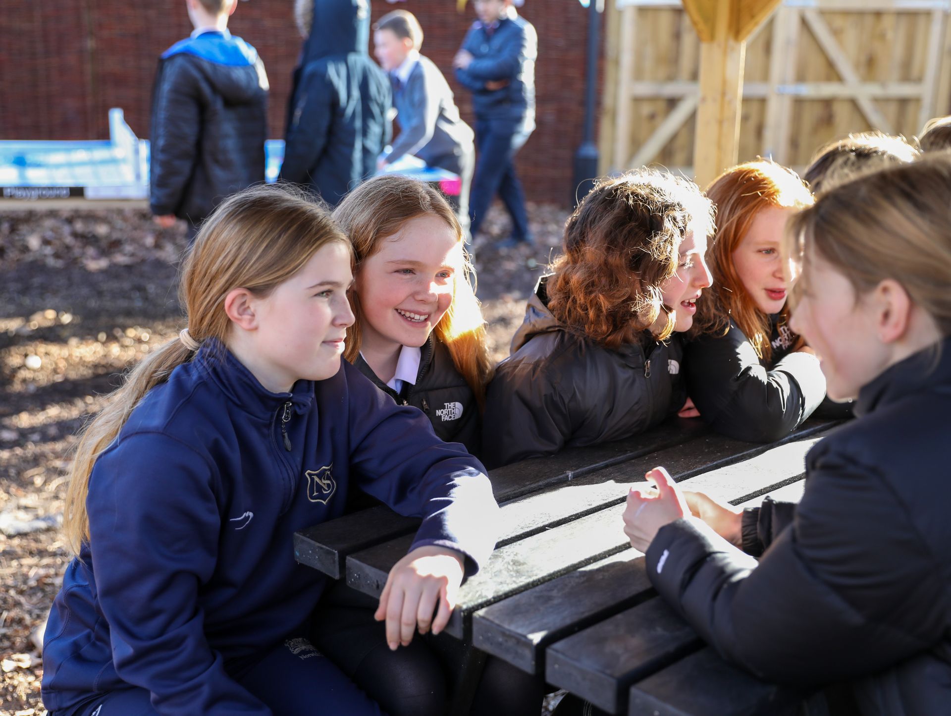 A group of young girls are sitting at a picnic table talking to each other.