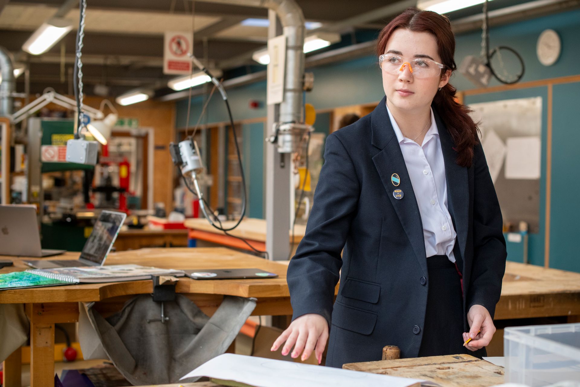 A woman in a suit and glasses is standing in a workshop.