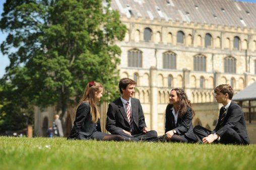 A group of students are sitting on the grass in front of a building.