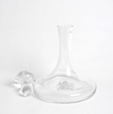 A clear glass decanter with a clear stopper on a white surface.