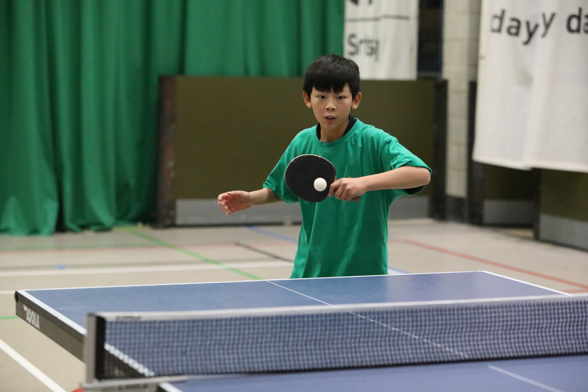 A young boy is playing ping pong on a table in a gym.