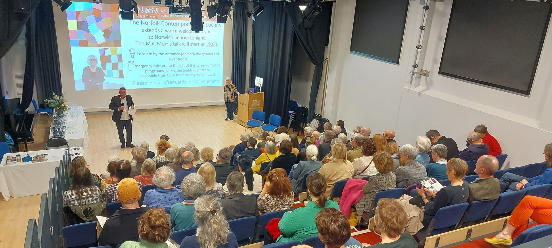 A large group of people are sitting in an auditorium watching a presentation.