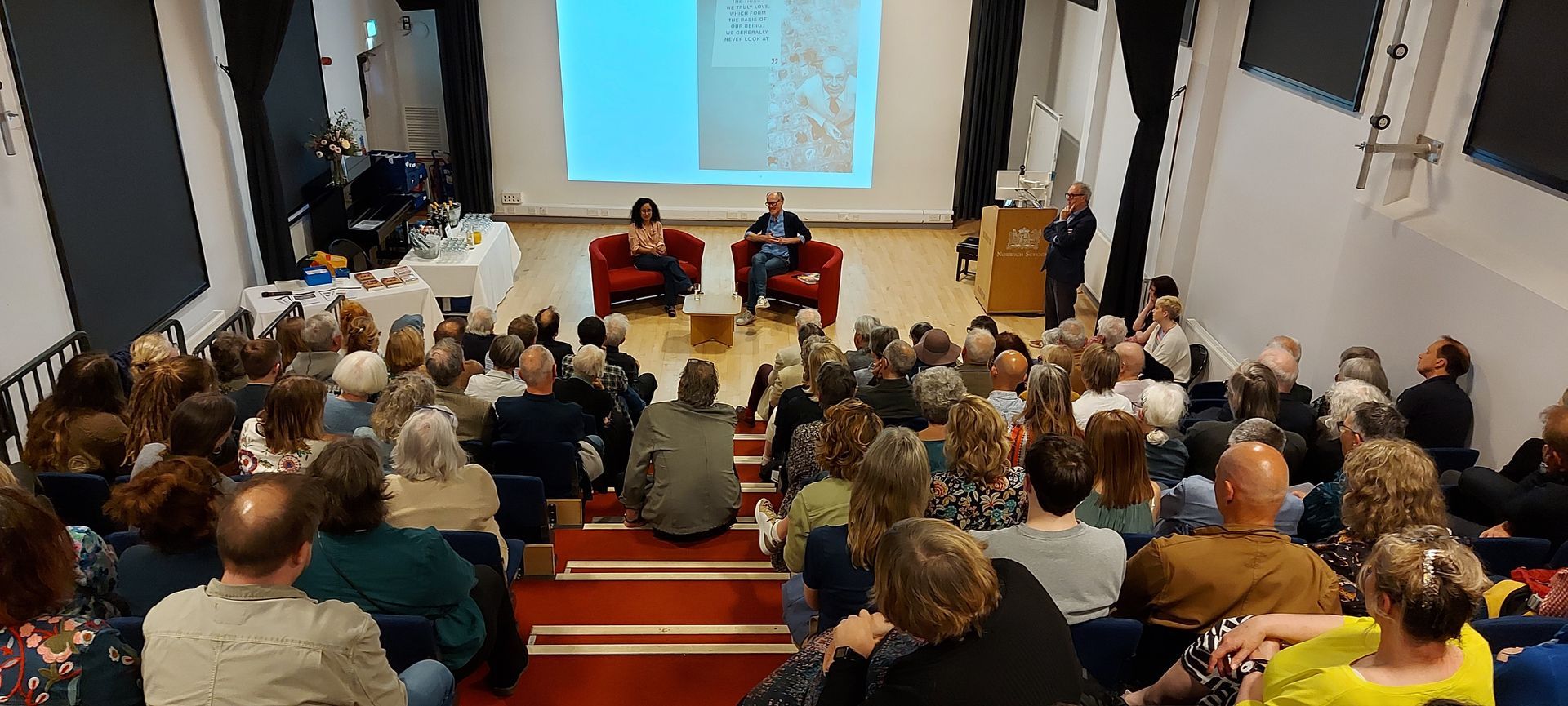 A large group of people are sitting in an auditorium watching a presentation.