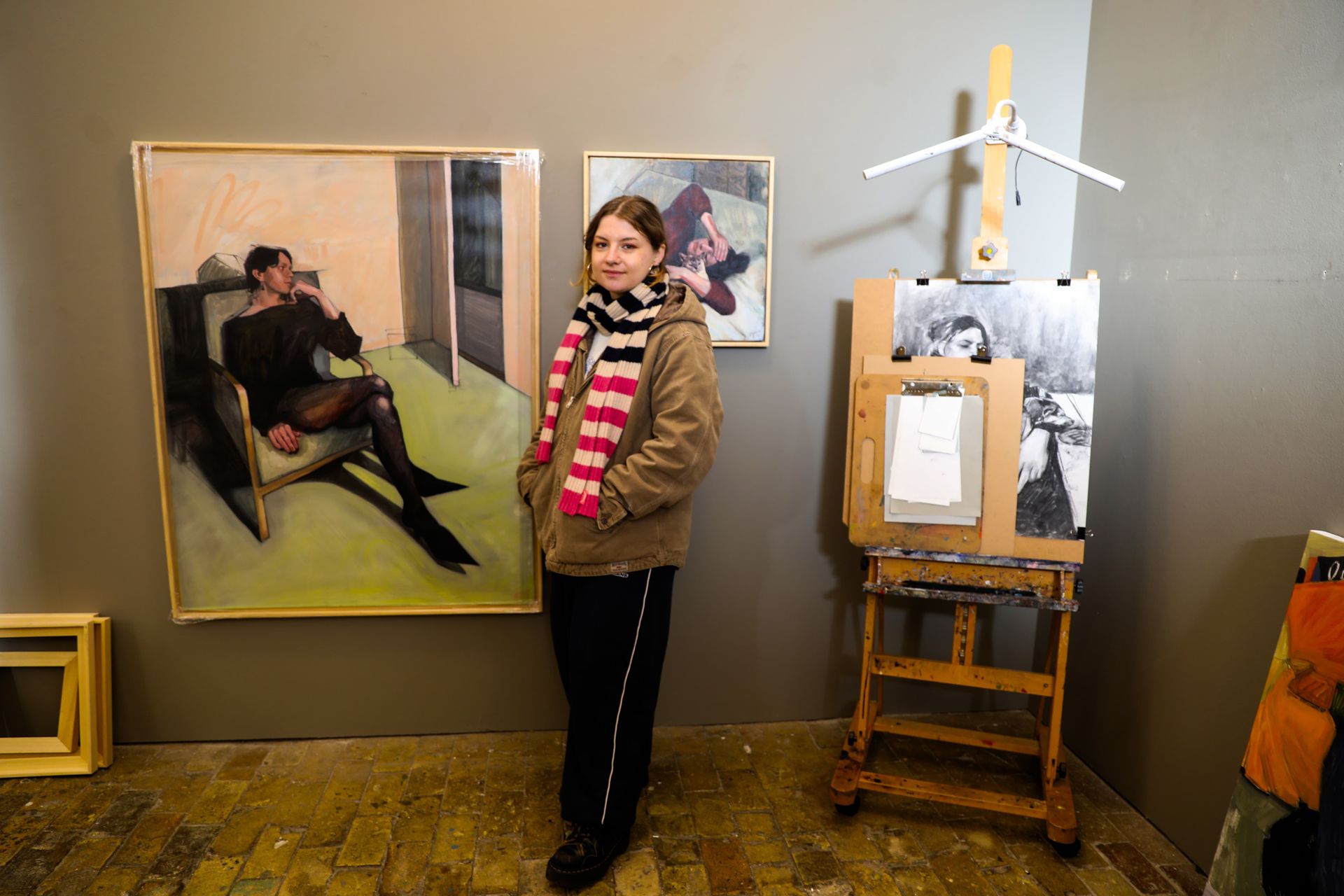 A woman is standing in a room with paintings on the wall and an easel.