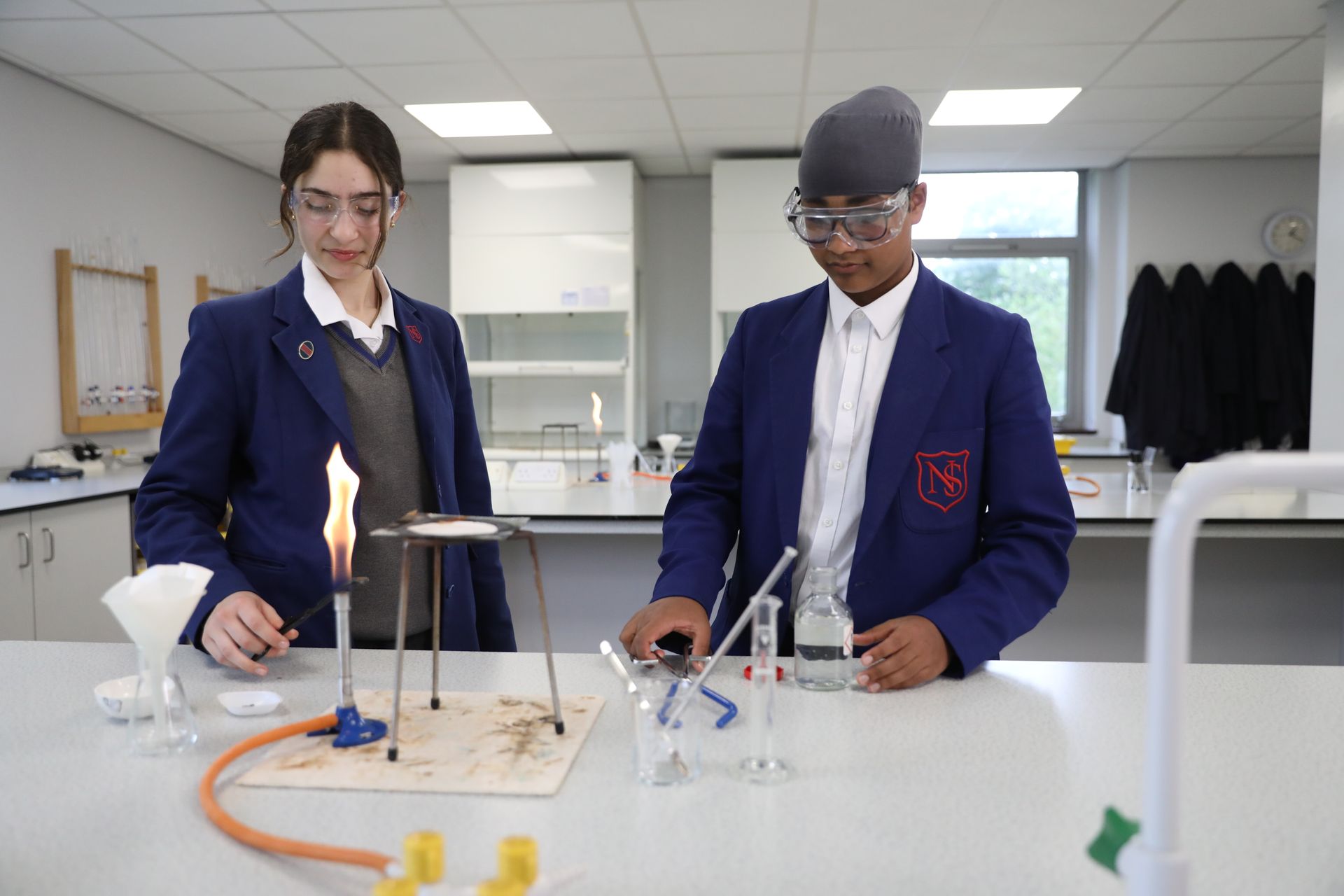 Two young boys are sitting at desks in a classroom using tablets.