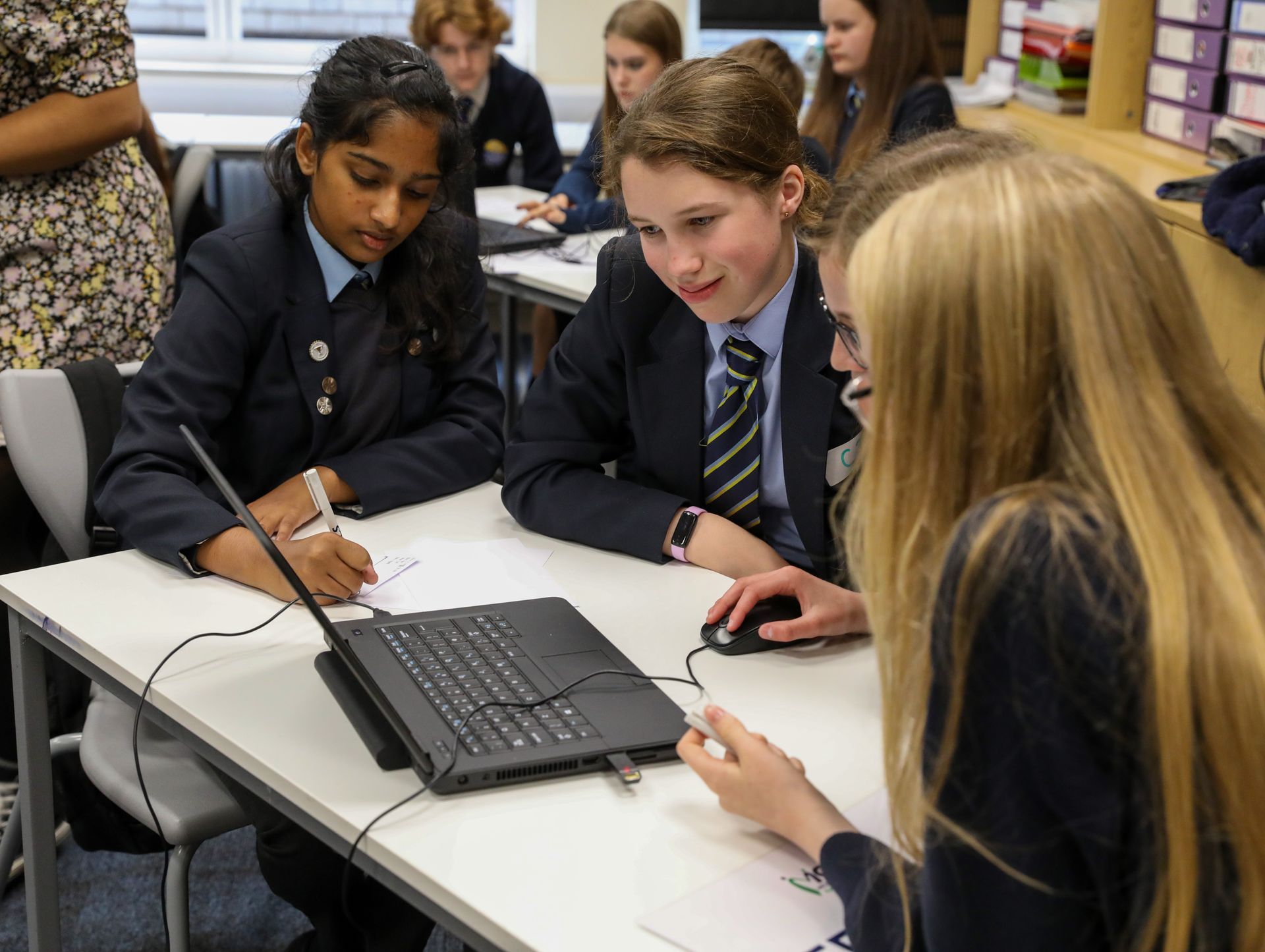 A group of students are sitting at a table looking at a laptop computer.