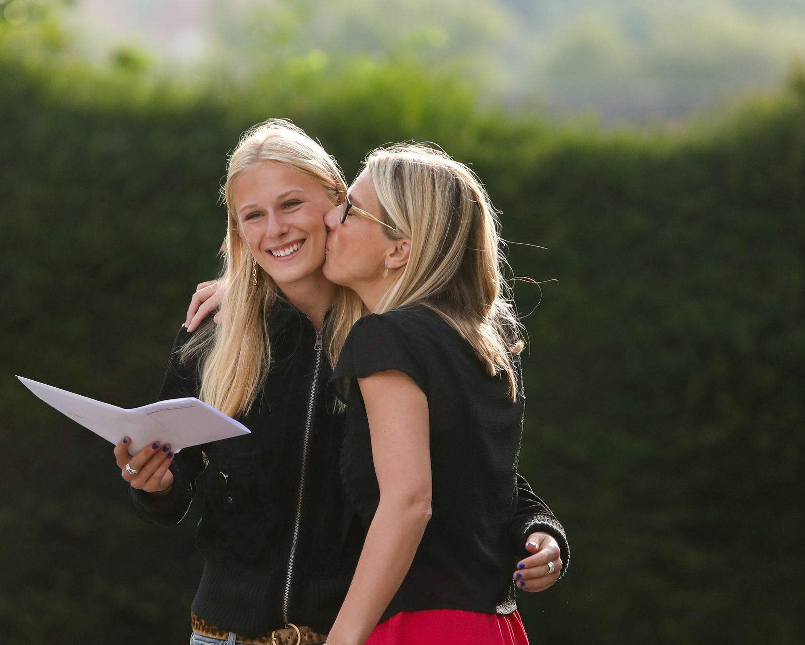 A woman kisses another woman on the cheek while holding a piece of paper