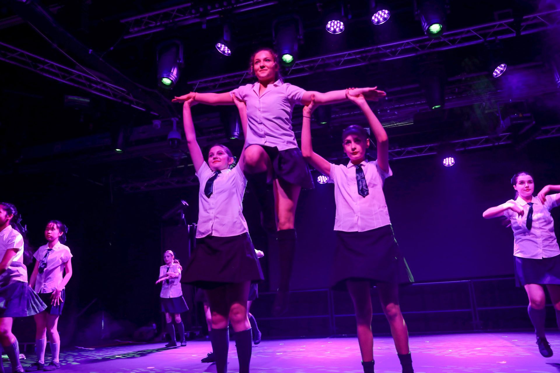 A group of girls are dancing on a stage with purple lights.