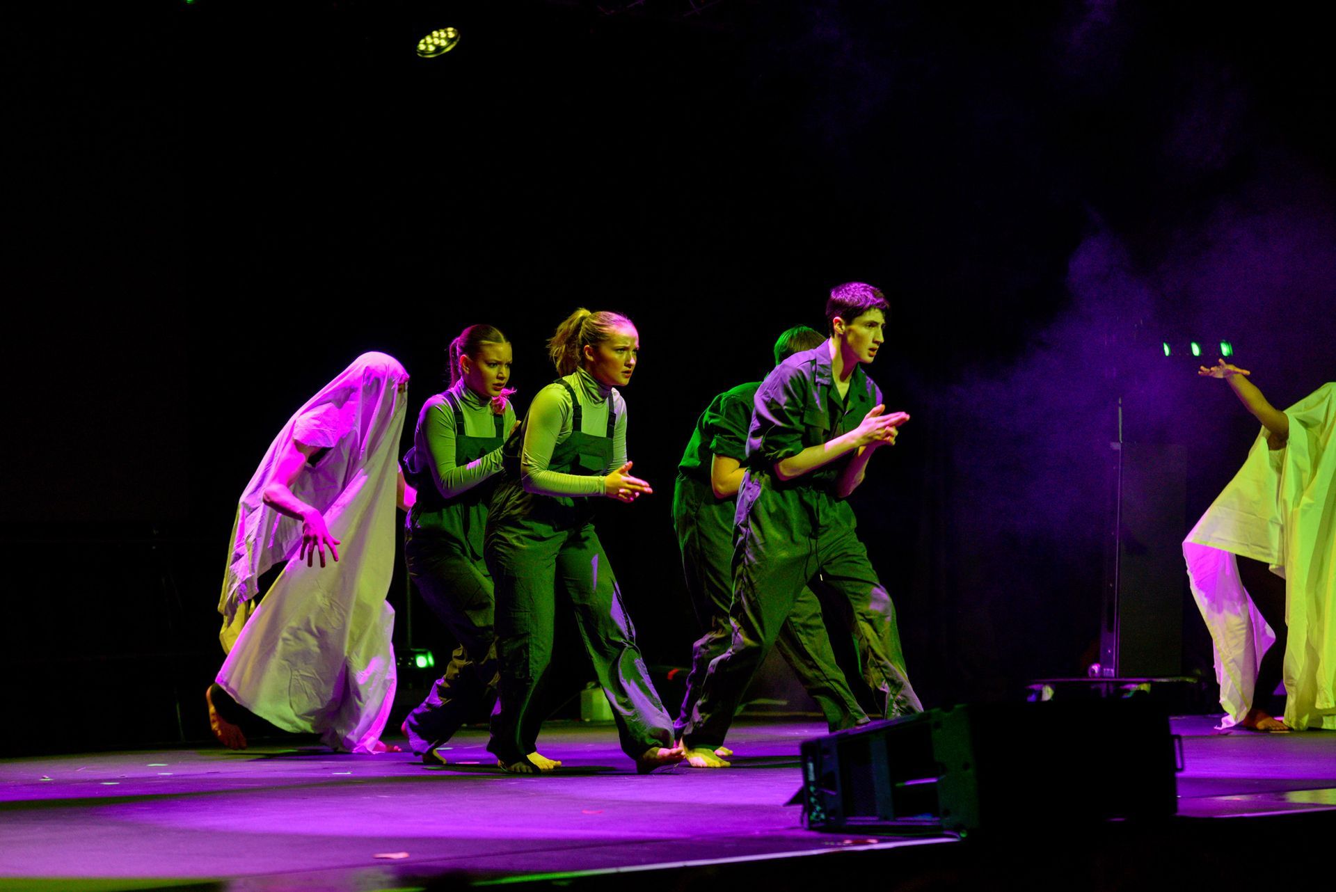 A group of people are dancing on a stage with purple lights.