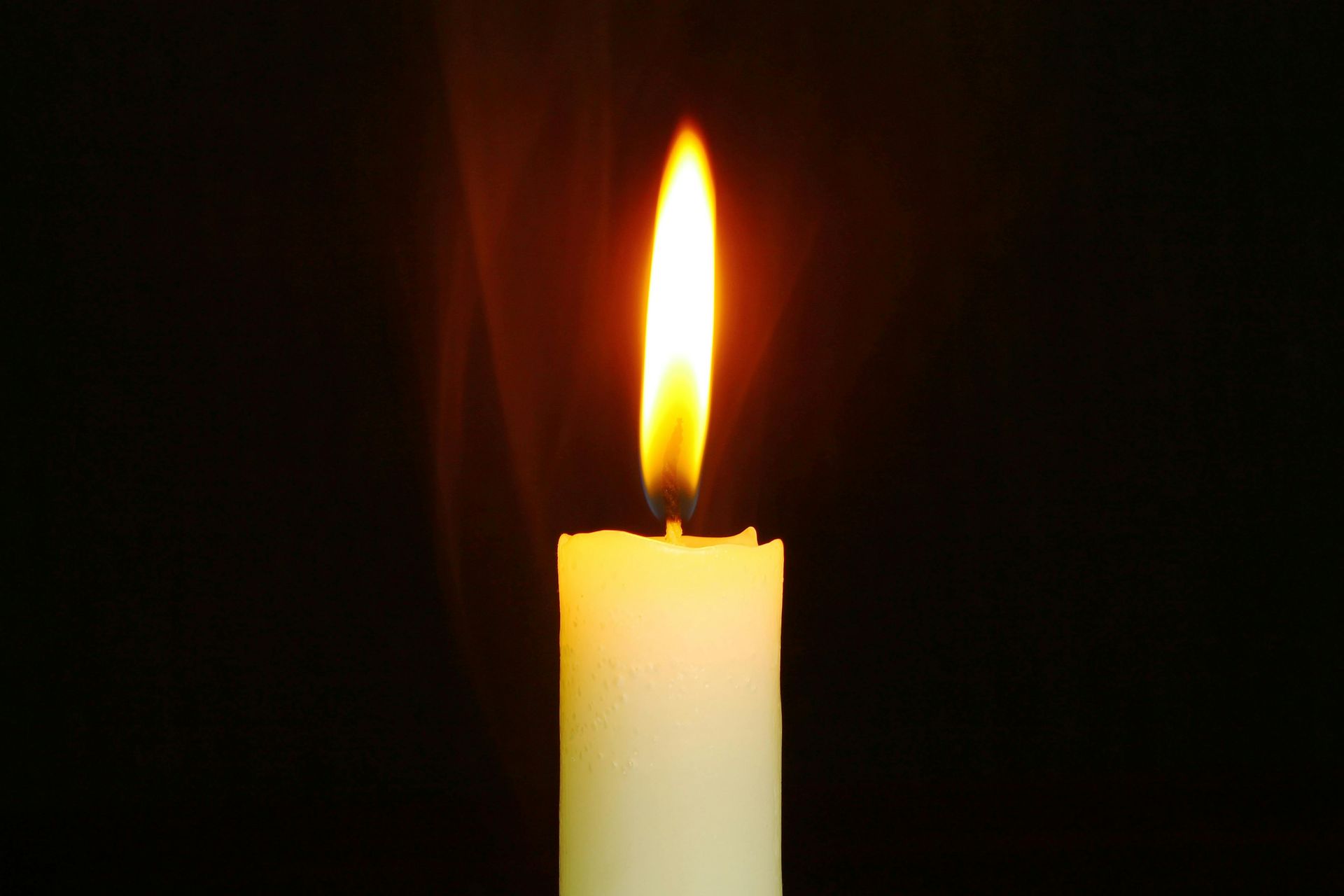 A single white candle is lit in the dark.