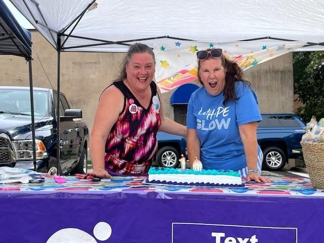 Two women standing in front of a table with a cake and a sign that says text