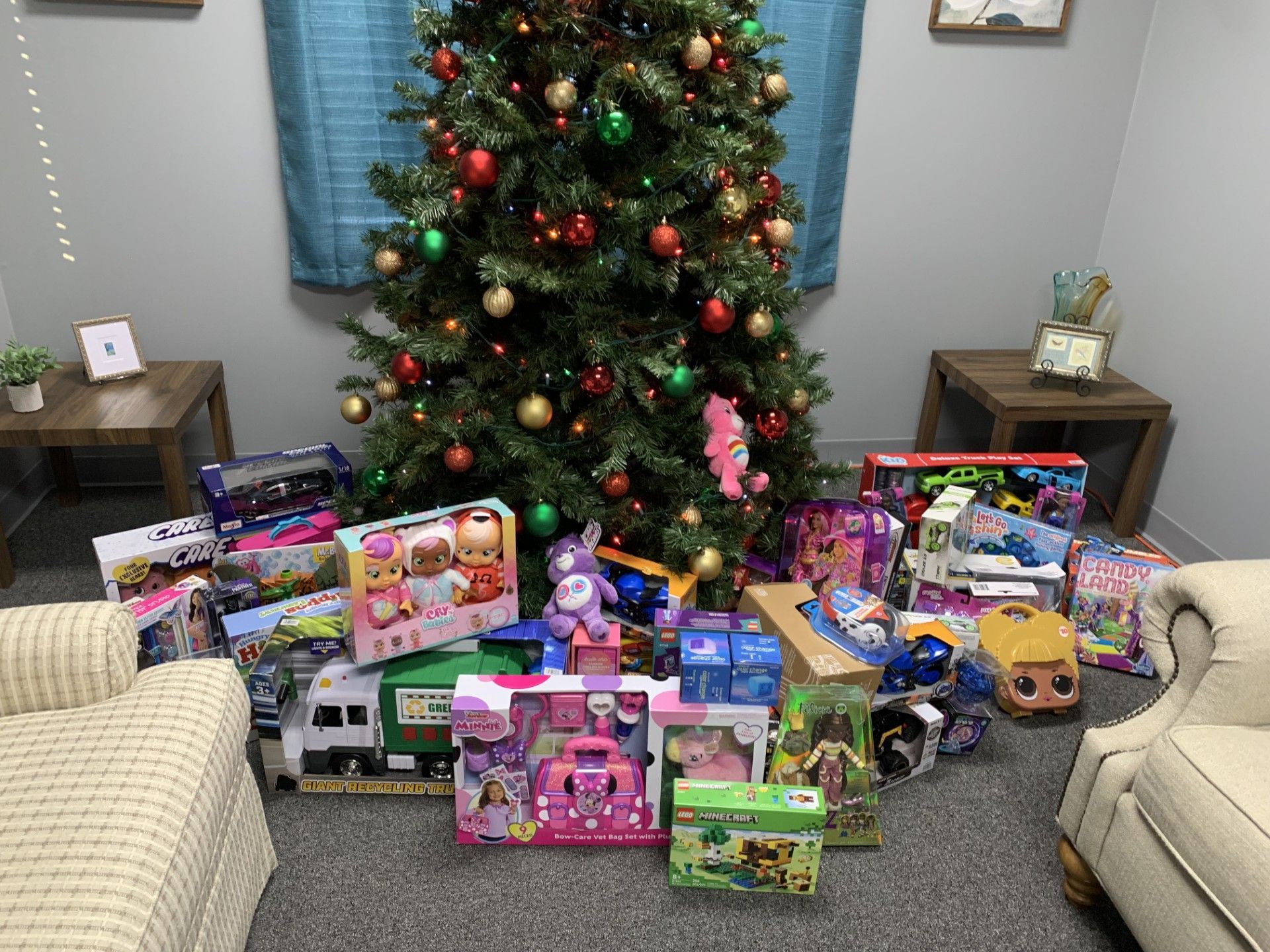 Christmas tree with toys in front, a chair on the left, and two small tables.