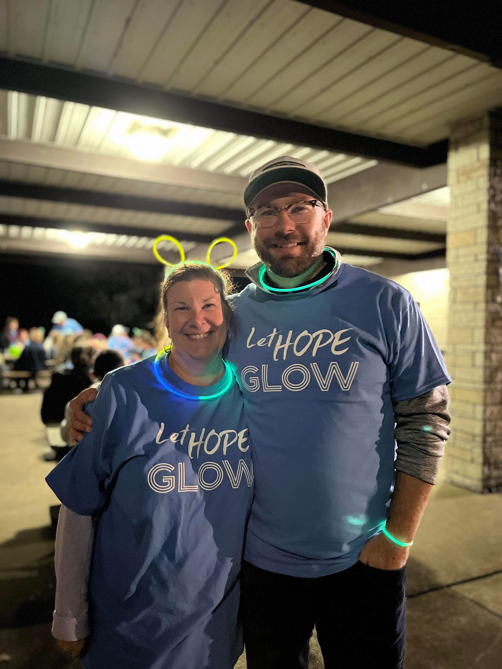 A man and a woman wearing glow in the dark shirts are posing for a picture.