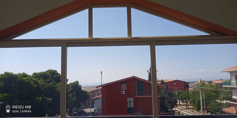 Edifici dai tetti rossi visti attraverso la struttura di un padiglione di legno sotto un cielo azzurro e limpido.