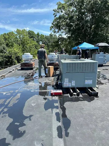 Workers stand on a flat commercial roof next to large HVAC units on a sunny day.