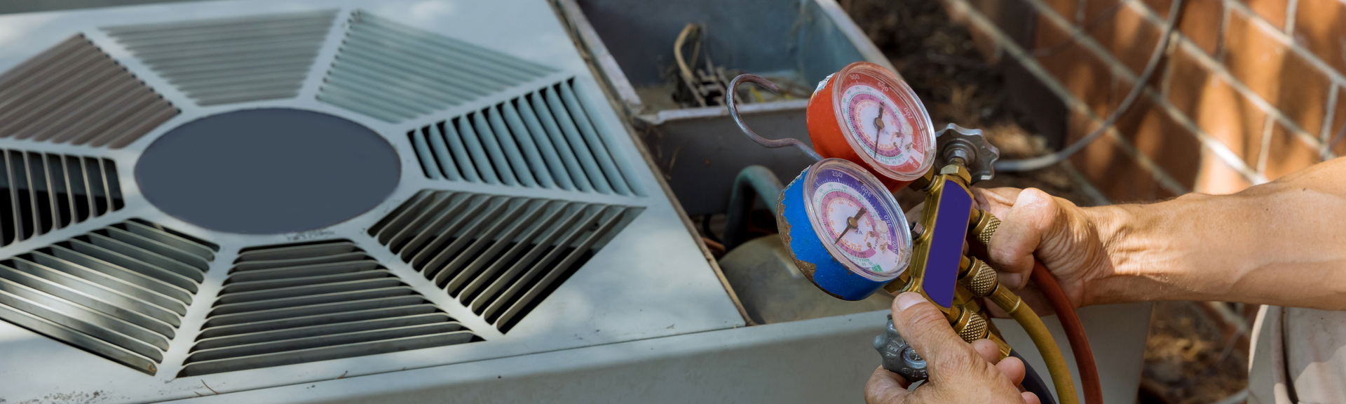 A technician uses a manifold gauge set to check the pressure of an outdoor residential air conditioning unit.
