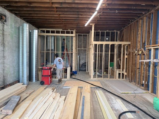 Construction workers build interior wood framing in an open, unfinished space with exposed joists and ductwork.