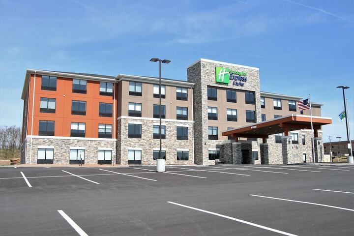 A multi-story Holiday Inn Express hotel with stone and tan siding, featuring a paved parking lot under a blue sky.