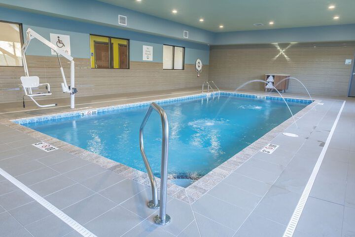 Indoor swimming pool with blue water, tiled deck, fountain jets, and a white accessibility lift chair.