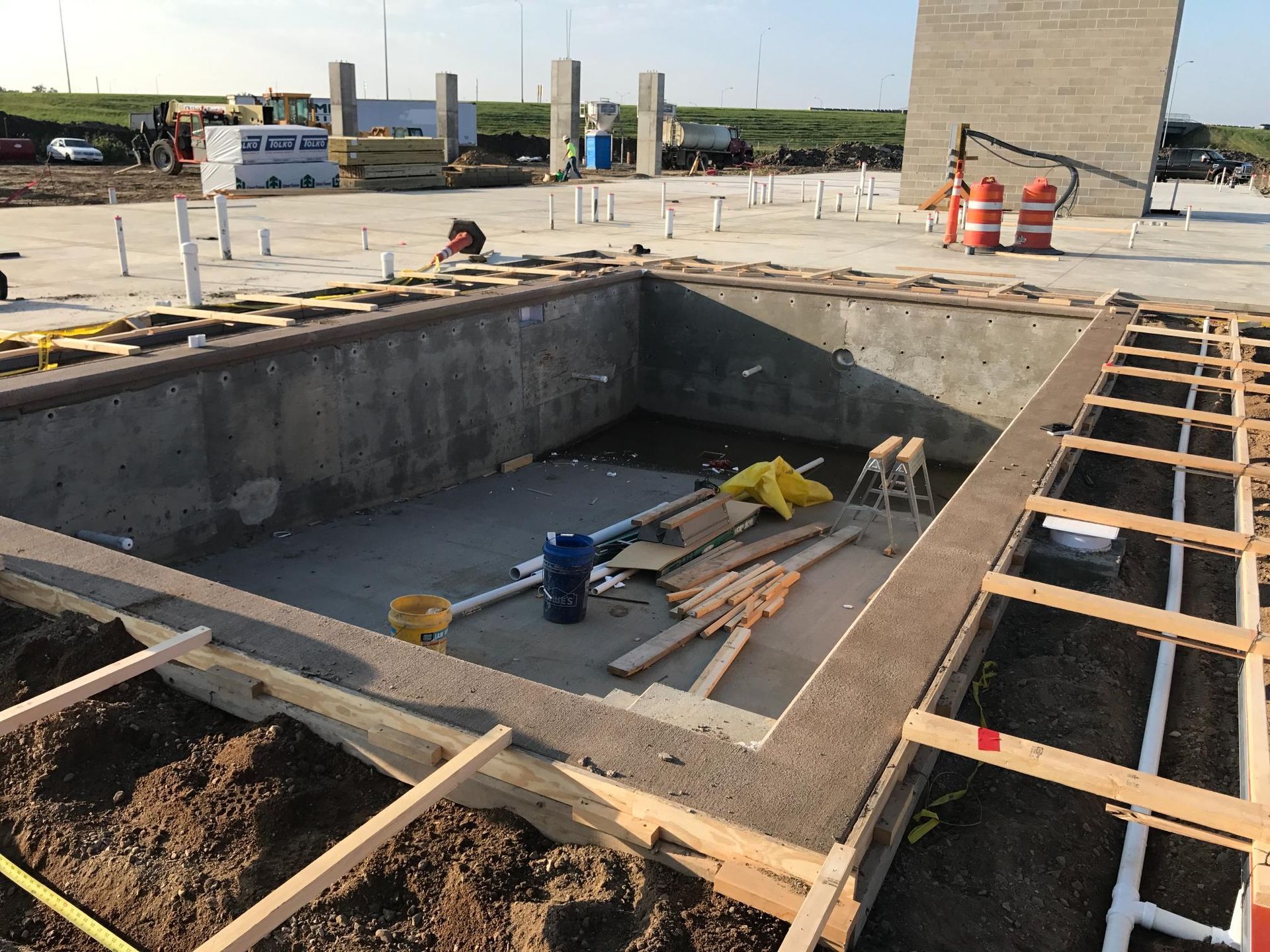Construction site with a concrete pit, wooden formwork, and orange safety barrels nearby