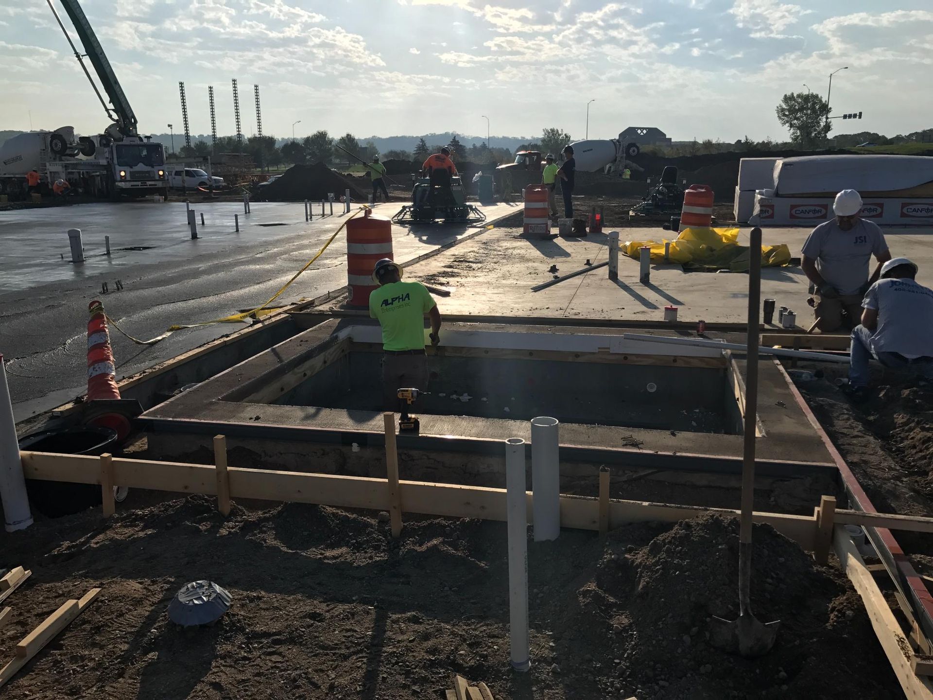 Construction workers at a wet roadwork site with a large open trench and barriers