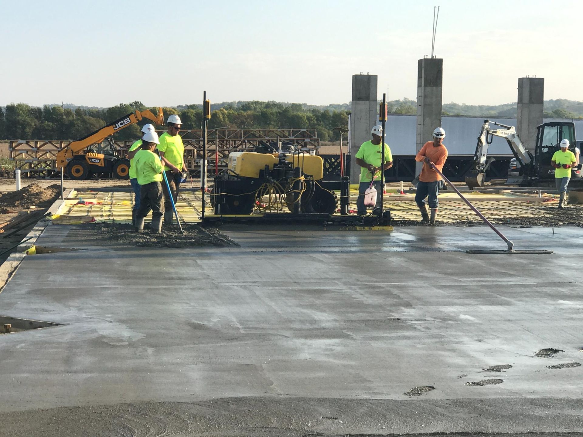 Workers paving a concrete surface at a construction site, with machinery and equipment in the background.