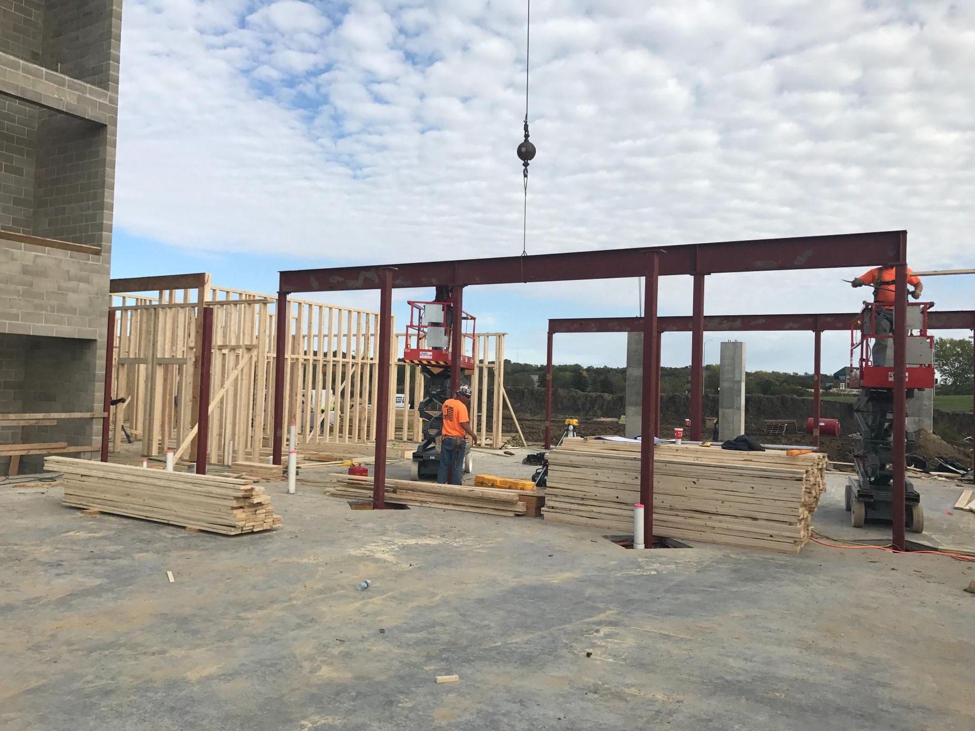 Construction site with steel frame, workers, and stacked lumber beside a concrete building