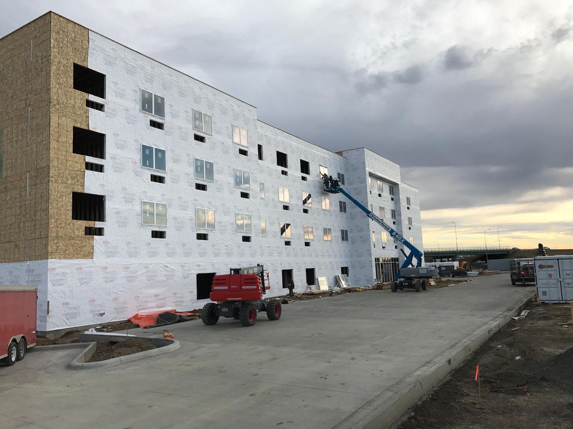 Apartment building under construction with lift, trucks, and cloudy sky