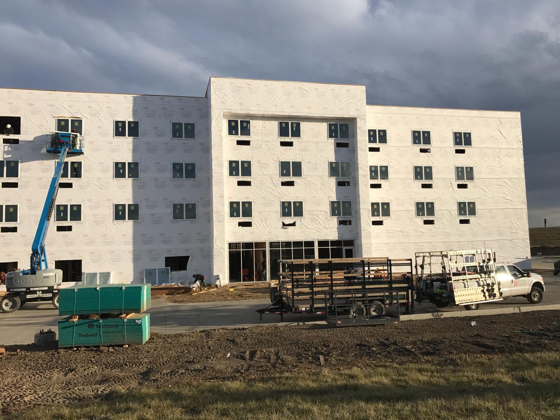 White multi-story building under construction with a blue lift, parked truck, and materials in front