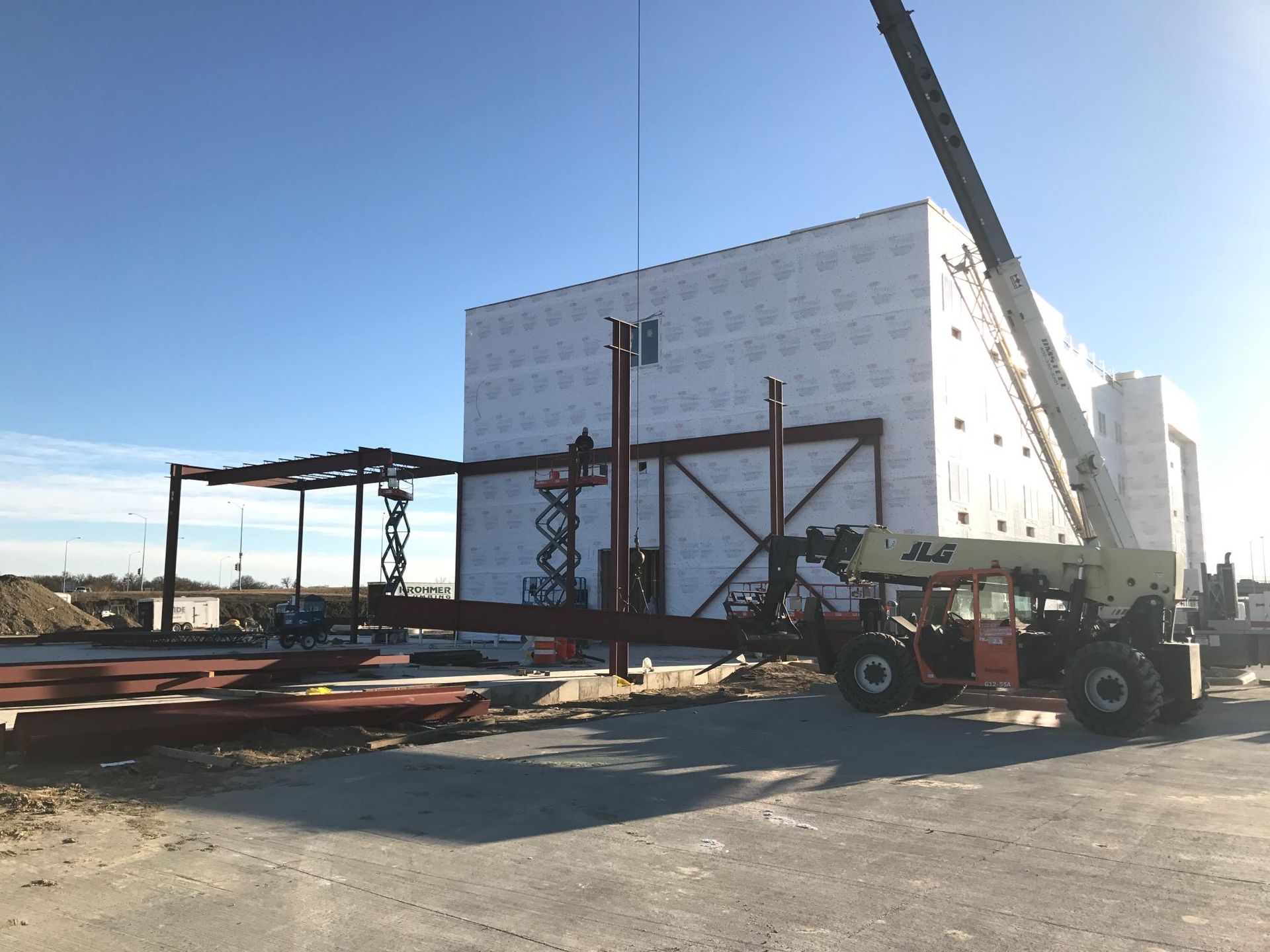 Construction site with steel frame, white building, and forklift under a clear blue sky