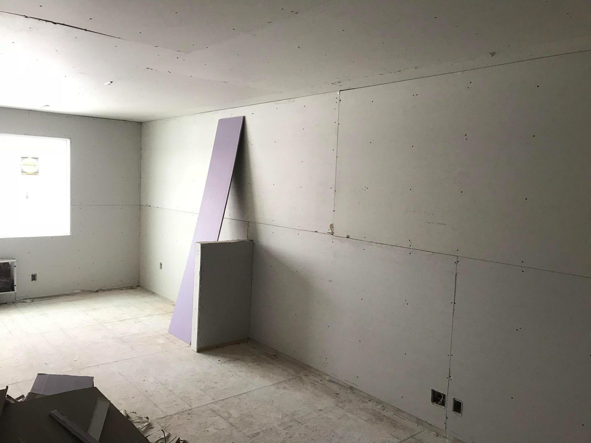 Unfinished room with drywall, a window, and a purple slanted structure against the wall.