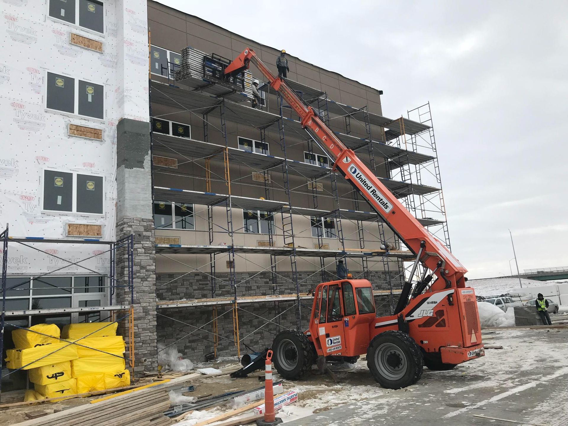 Orange telehandler lifting debris from a damaged building under demolition