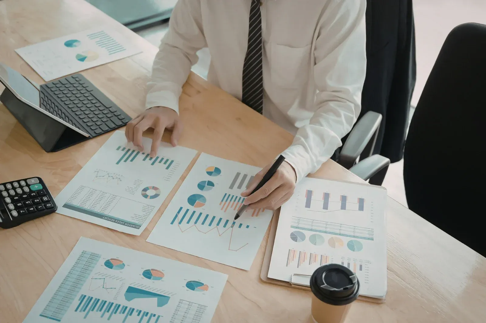 Professional sits at a desk reviewing multiple printed financial charts and graphs with a pen.