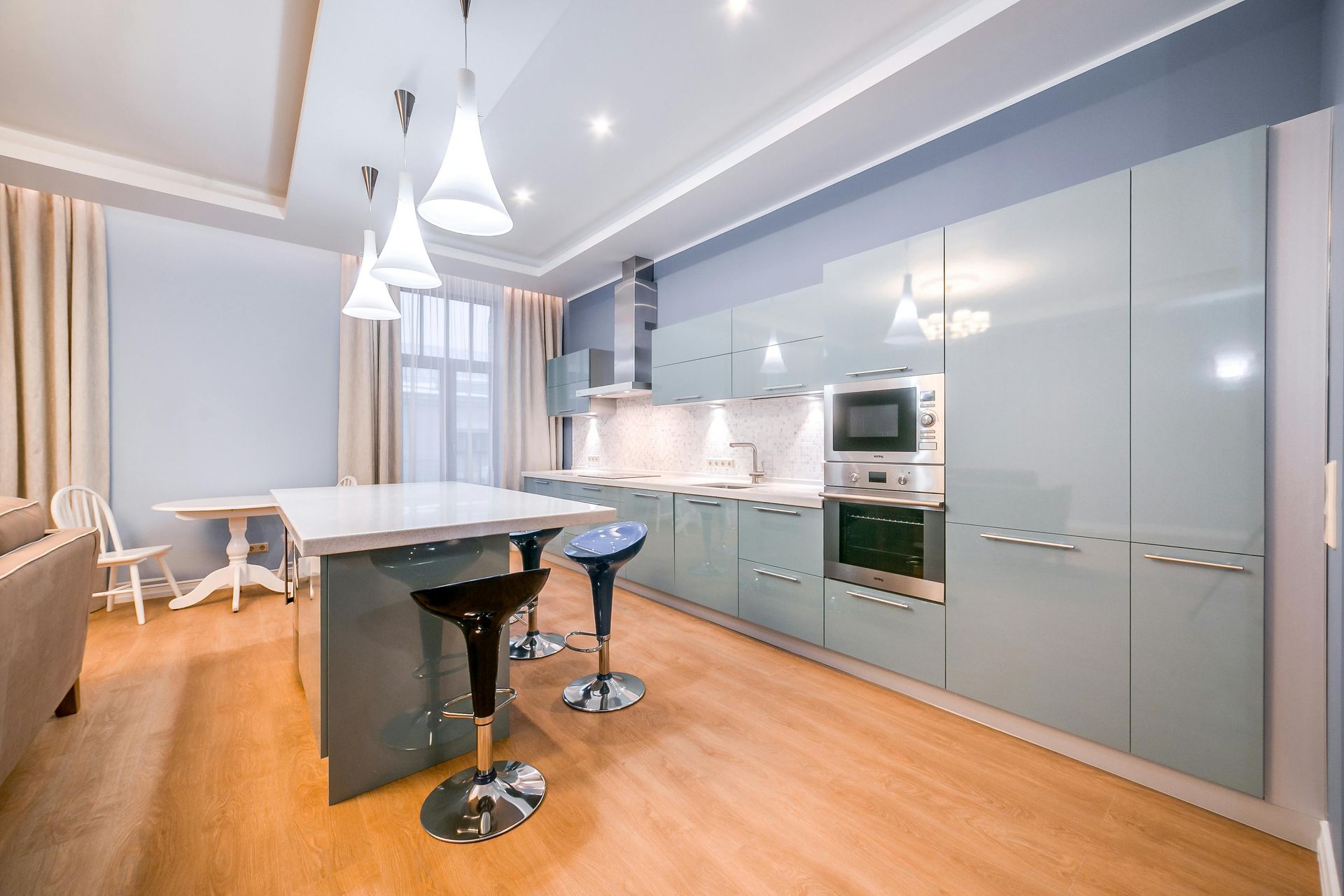 Modern kitchen with light blue glossy cabinets, a central island with bar stools, and warm wood flooring.