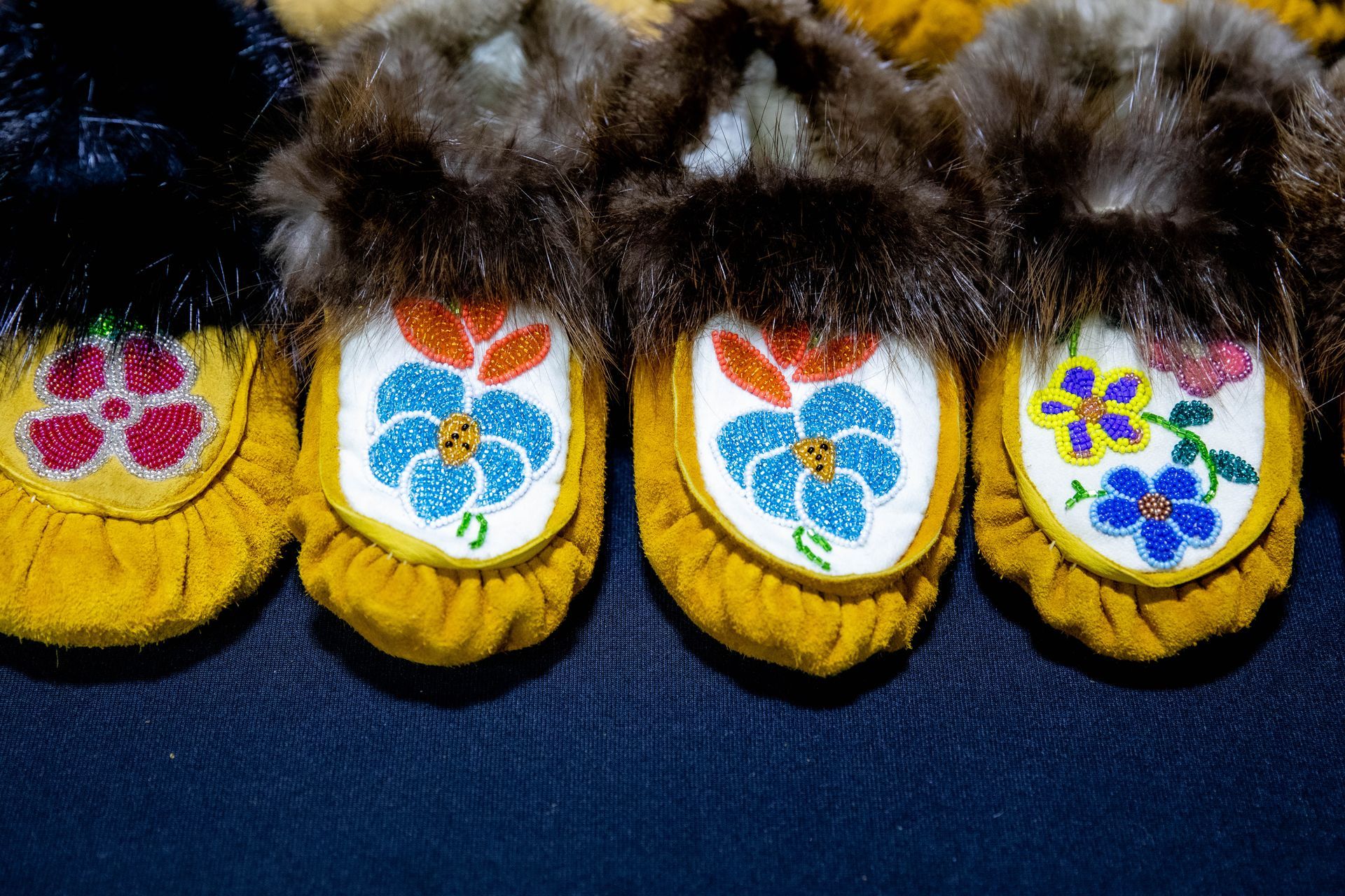 Close-up of four yellow moccasins with beaded floral designs and fur trim.