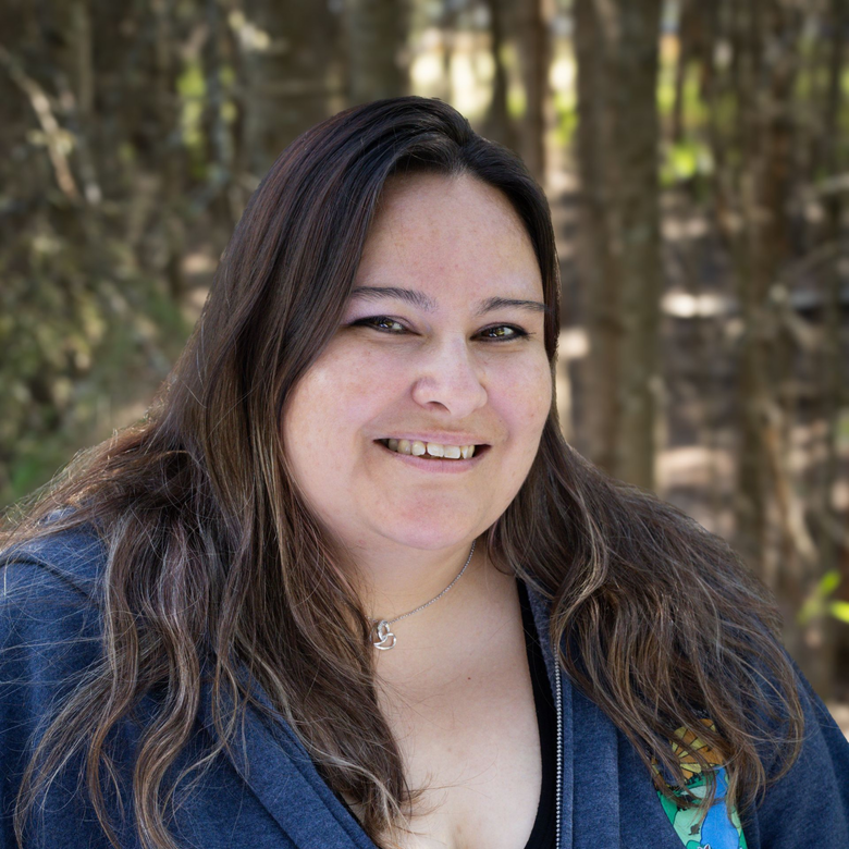Woman with gray hair smiles, wearing a gray and white patterned sweater; outdoor background.