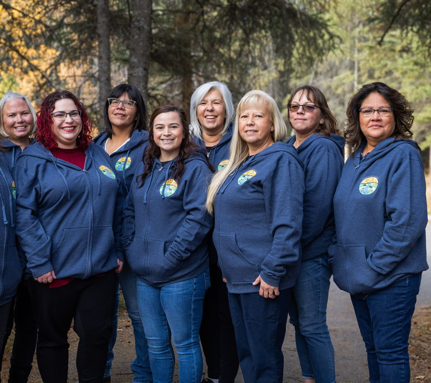 Group of women wearing blue hoodies, standing outdoors on a path, smiling.