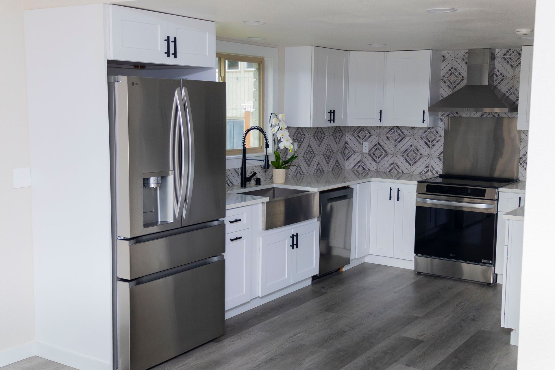 A modern kitchen with white cabinets, stainless steel appliances, a farmhouse sink, and geometric patterned tile backsplash.