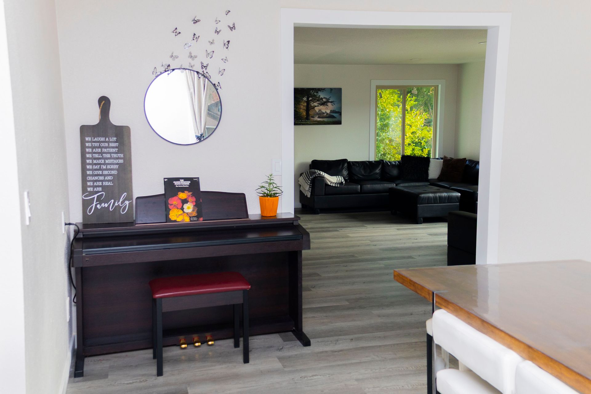 A dark wood piano with a red bench sits against a wall with a round mirror and wall art, opening into a living room.