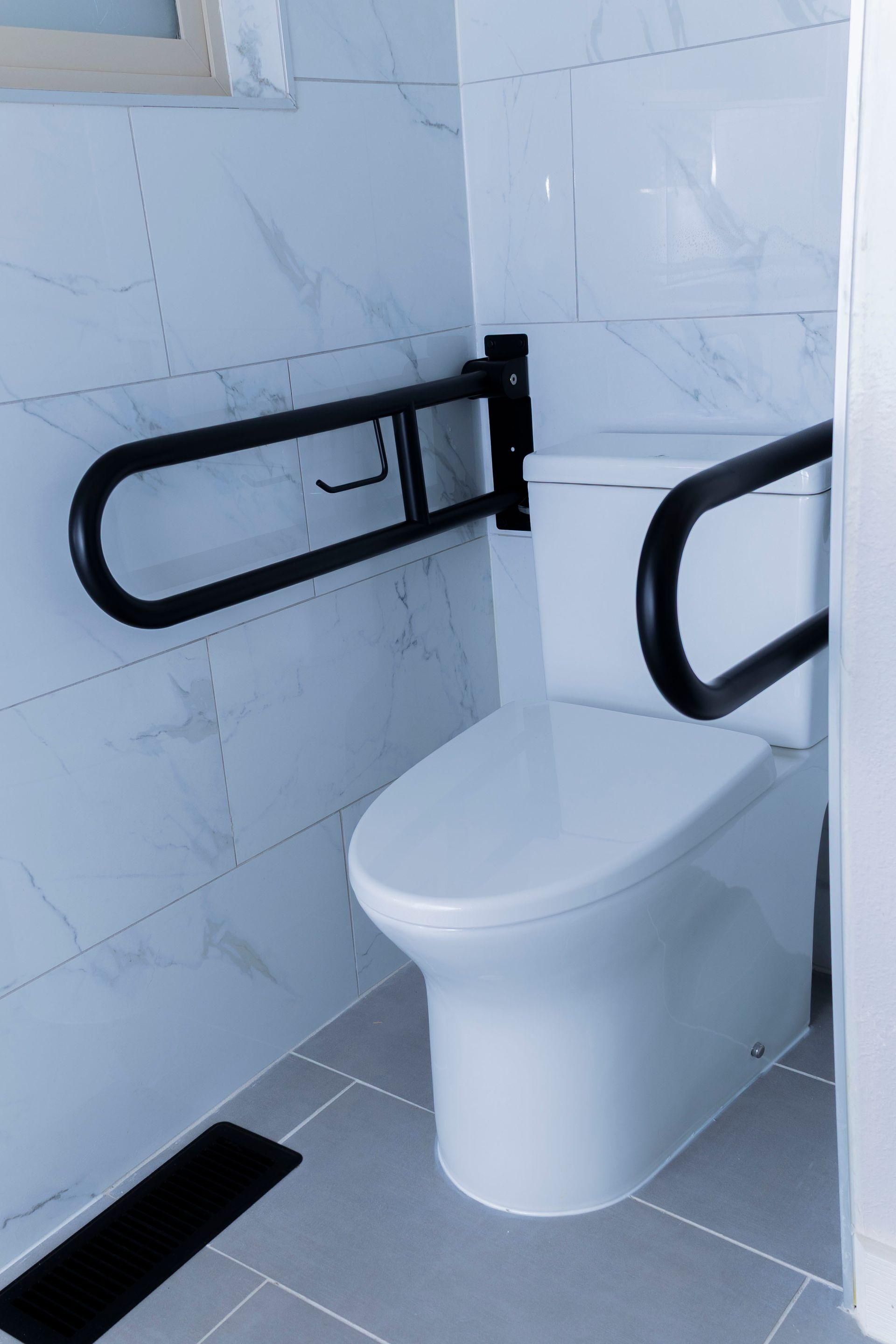 A white toilet in a tiled bathroom with two black, wall-mounted safety grab bars on either side.